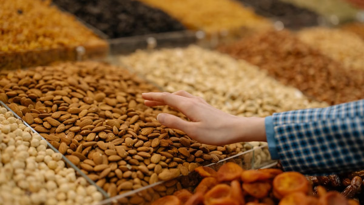 Hand reaching for almonds in a colorful dry food market display, highlighting freshness.